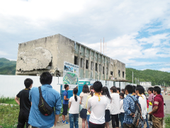 A group of students listening to a guide in front of a tsunami-damaged building during a field trip.
