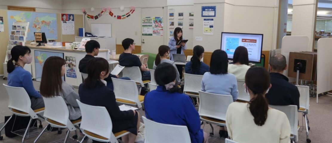 定期開催イベントの写真。女性がスライドを使って発表しているのを12人の人が聞いている。